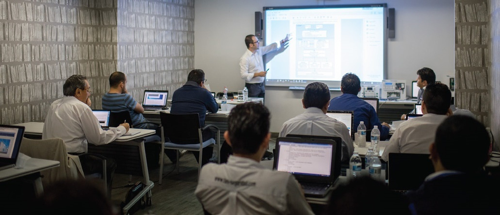 Un instructor presenta contenido técnico ante participantes con computadoras.